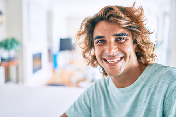 Junger hispanischer Mann lächelt glücklich auf dem Tisch zu Hause - Foto, Bild
