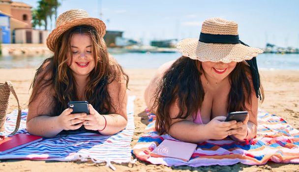 Dvě plus velikost nadváha sestry dvojčata ženy ležící na pláži s chytrým telefonem o letních prázdninách - Fotografie, Obrázek