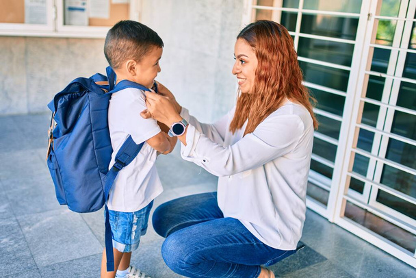 Adorable latin student boy and mom at school. Mother preparing kid putting up backpack. - Photo, Image