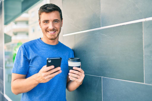 Молодой кавказский мужчина, пользующийся смартфоном и выпивший кофе, уносит в город. - Фото, изображение