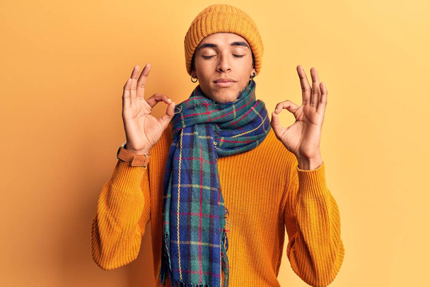 Mladý afroameričan v neformálním zimním oblečení se uvolní a usměje se se zavřenýma očima, dělá meditační gesto prsty. koncepce jógy.  - Fotografie, Obrázek