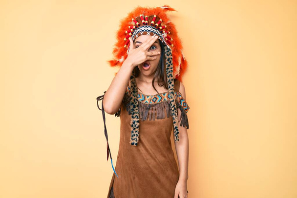 Giovane bella ragazza latina con indosso costume indiano sbirciare in shock che copre il viso e gli occhi con la mano, guardando attraverso le dita con espressione imbarazzata.  - Foto, immagini