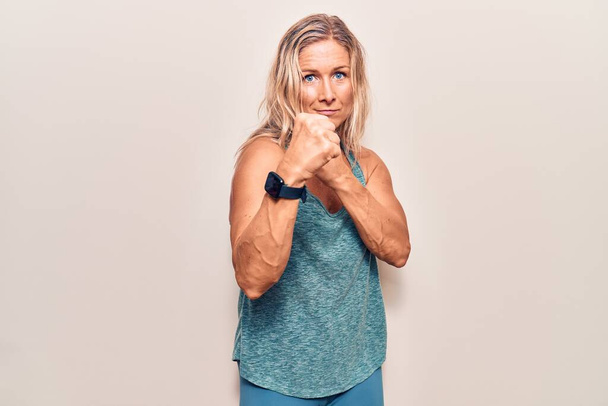 Middle age caucasian blonde woman wearing sportswear ready to fight with fist defense gesture, angry and upset face, afraid of problem  - Photo, Image