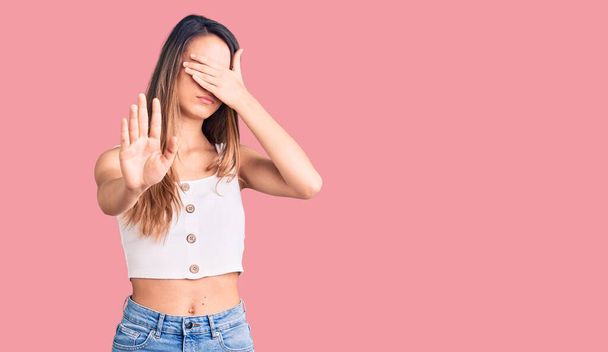 Young beautiful girl wearing casual sleeveless t shirt covering eyes with hands and doing stop gesture with sad and fear expression. embarrassed and negative concept.  - Photo, Image