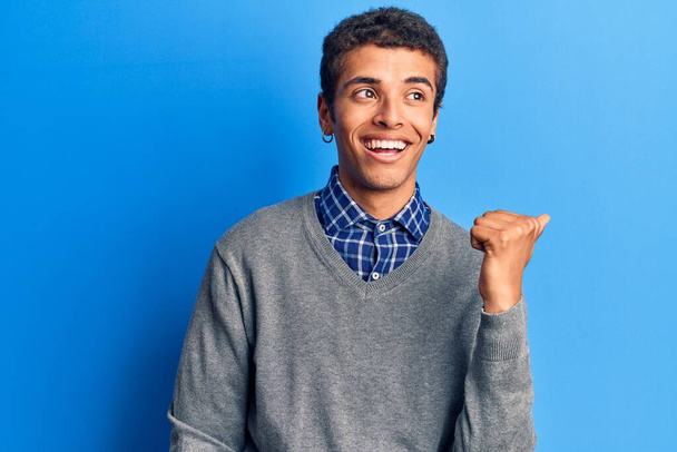 Junger afrikanisch-amerikanischer Mann in lässiger Kleidung lächelt mit glücklichem Gesicht und zeigt mit erhobenem Daumen zur Seite.  - Foto, Bild