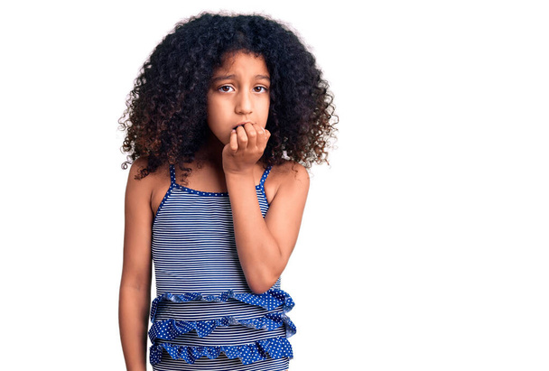 Mayo giyen kıvırcık saçlı Afro-Amerikalı çocuk gergin görünüyor ve elleri dudağında tırnak yiyor. anksiyete.  - Fotoğraf, Görsel