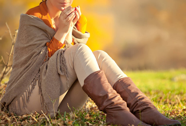 Una mujer en ropa de punto caliente bebe una taza de té caliente o café al aire libre a la luz del sol.. - Foto, Imagen