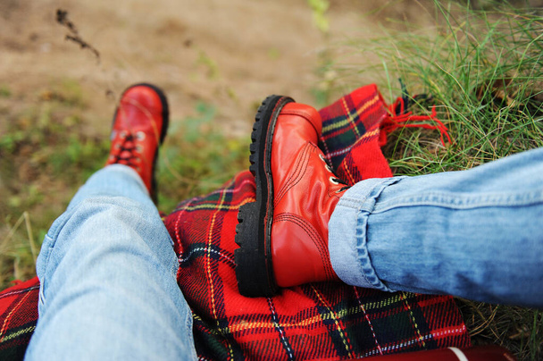 Tourism aesthetic. Red boots, checkered plaid in autumn nature, legs closeup - Photo, Image