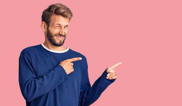 Handsome blond man with beard wearing casual sweater pointing aside worried and nervous with both hands, concerned and surprised expression  - Photo, Image