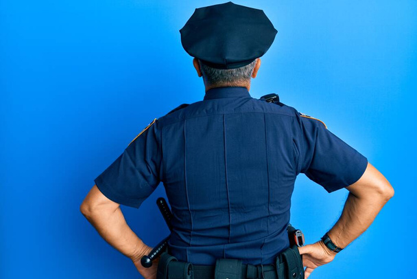 Handsome middle age mature man wearing police uniform standing backwards looking away with arms on body  - Foto, Bild