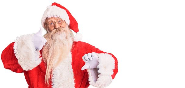 Старий старший чоловік з сірим волоссям і довгою бородою в традиційному костюмі Санта-Клауса робить великі пальці вгору і вниз, розбіжності і вираження згоди. божевільний конфлікт
  - Фото, зображення
