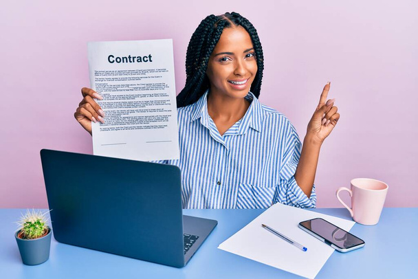 Beautiful hispanic woman at the office showing contract document smiling happy pointing with hand and finger to the side  - Фото, изображение