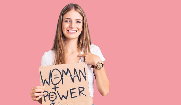 Young beautiful blonde woman holding woman power banner pointing finger to one self smiling happy and proud  - Foto, imagen