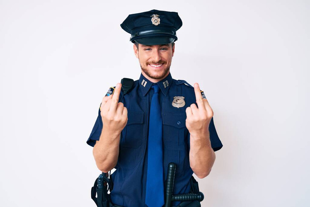 Young caucasian man wearing police uniform showing middle finger doing fuck you bad expression, provocation and rude attitude. screaming excited  - Fotó, kép