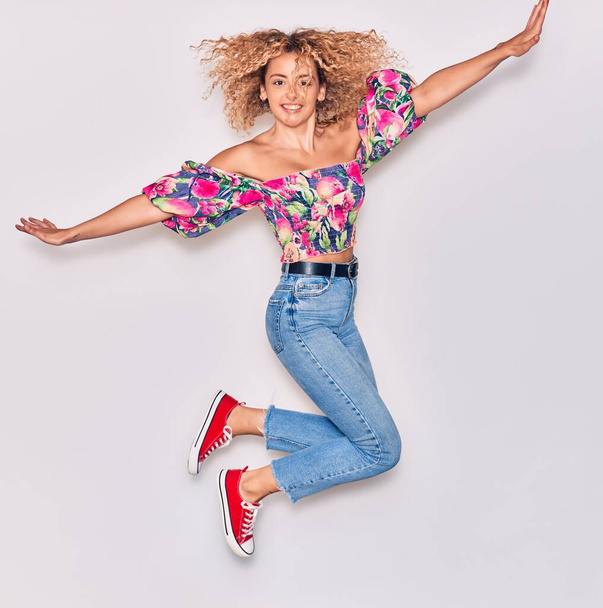 Young beautiful curly girl wearing casual clothes smiling happy. Jumping with smile on face and arms opened over isolated white background. - Photo, Image