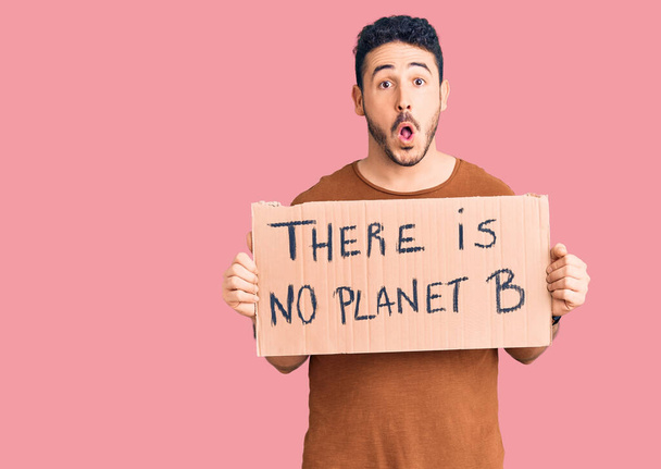 Young hispanic man holding there is no planet b banner scared and amazed with open mouth for surprise, disbelief face  - Photo, Image