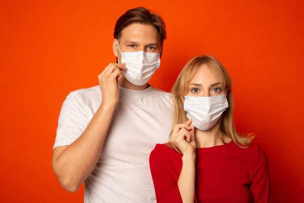 beautiful young couple, female and male in medical masks on a red background - Zdjęcie, obraz