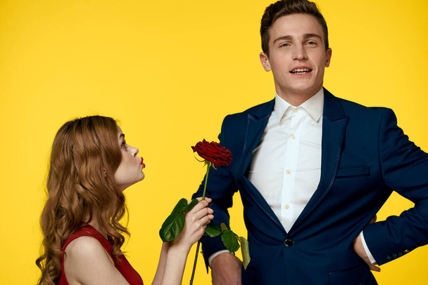 Ein romantischer Mann umarmt eine Frau in einem roten Kleid mit einer Rose in der Hand auf gelbem Hintergrund - Foto, Bild
