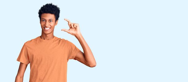 Young african american man wearing casual clothes smiling and confident gesturing with hand doing small size sign with fingers looking and the camera. measure concept.  - Photo, Image