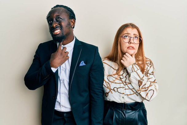 Young interracial couple wearing business and elegant clothes thinking worried about a question, concerned and nervous with hand on chin  - Foto, afbeelding