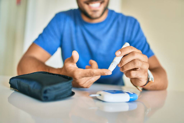 Νεαρός ισπανόφωνος διαβητικός άνδρας που μετρά τα επίπεδα γλυκόζης στο σπίτι - Φωτογραφία, εικόνα