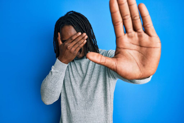 Afroameričan s copánky na sobě rolák svetr zakrývající oči s rukama a dělat stop gesto se smutným a strach výraz. trapný a negativní koncept.  - Fotografie, Obrázek