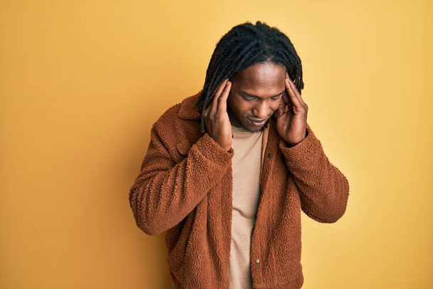 Afroamerikanischer Mann mit Zöpfen in brauner Retro-Jacke, die Ohren mit Fingern bedeckt, die genervt sind von dem Lärm lauter Musik. Gehörloses Konzept.  - Foto, Bild