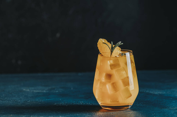 Yellow orange cocktail with tangerine and rosemary with ice in glass on dark blue concrete background , close up. Christmas and New Year holiday welcome drink - Photo, image