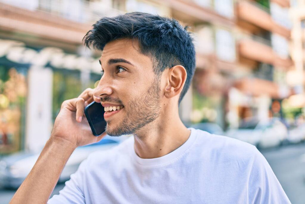 Giovane uomo latino sorridente felice parlando sullo smartphone a piedi in città. - Foto, immagini