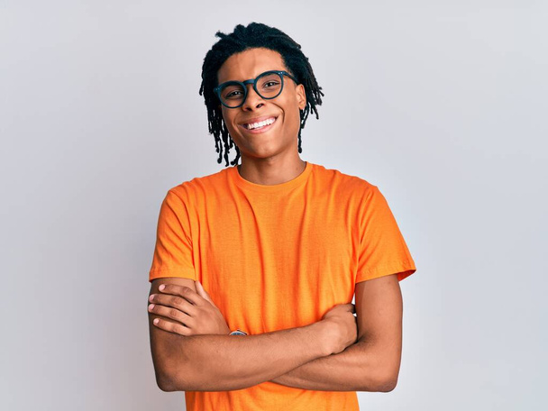 Jeune homme afro-américain portant des vêtements décontractés et des lunettes visage heureux souriant avec les bras croisés regardant la caméra. personne positive.  - Photo, image