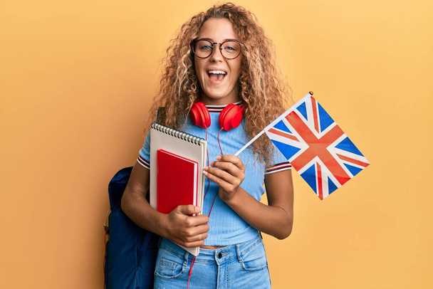 Gyönyörű kaukázusi tinédzser lány csere diák tartja UK zászló mosolyogva és nevetve keményen ki, mert vicces őrült vicc.  - Fotó, kép