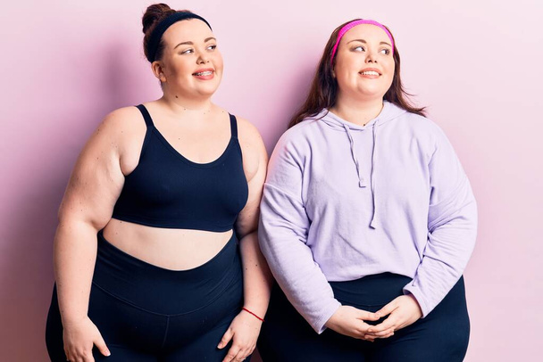 Young plus size twins wearing sportswear looking away to side with smile on face, natural expression. laughing confident.  - Fotografie, Obrázek
