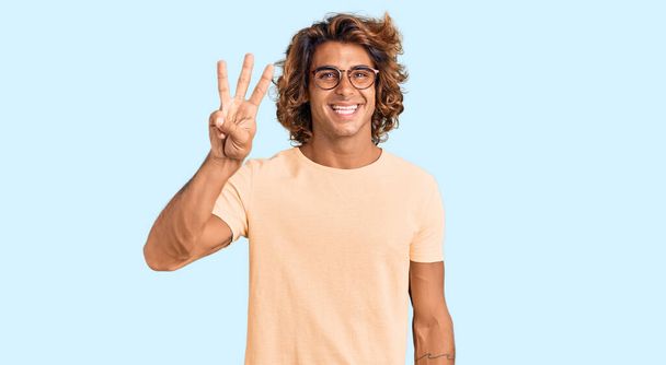 Mladý hispánec nosí ležérní oblečení a brýle ukazující a ukazující prsty číslo tři a usmívající se sebevědomě a šťastně.  - Fotografie, Obrázek