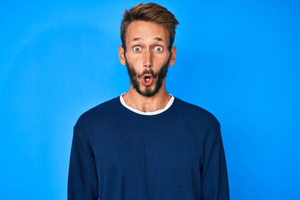 Handsome caucasian man with beard wearing casual sweater scared and amazed with open mouth for surprise, disbelief face  - Photo, Image