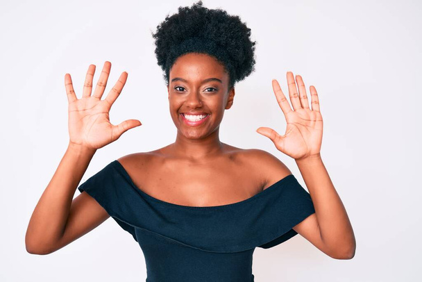 Junge afrikanisch-amerikanische Frau trägt lässige Kleidung und zeigt mit den Fingern Nummer zehn nach oben, während sie selbstbewusst und glücklich lächelt.  - Foto, Bild