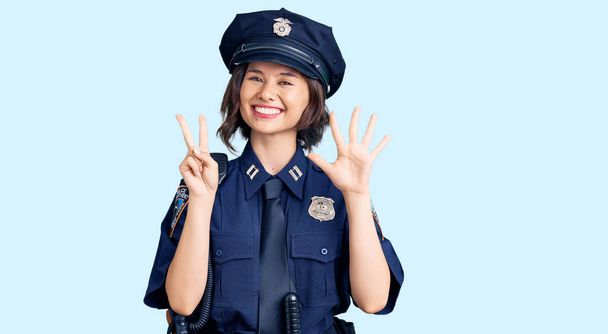 Mladá krásná dívka v policejní uniformě ukazuje a ukazuje s prsty číslo sedm a zároveň se usmívá sebevědomě a šťastně.  - Fotografie, Obrázek
