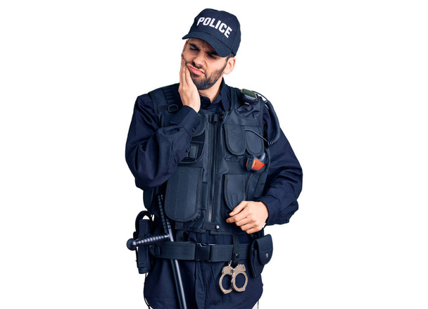 Young handsome man with beard wearing police uniform touching mouth with hand with painful expression because of toothache or dental illness on teeth. dentist  - Photo, Image