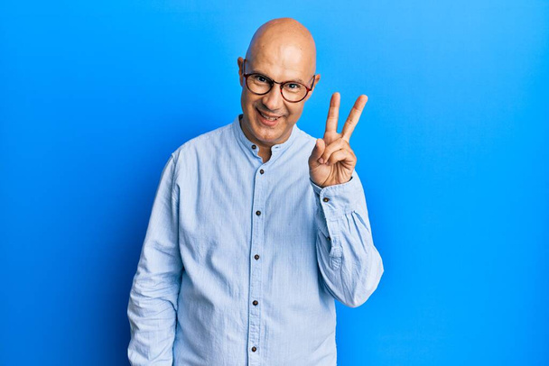 Middle age bald man wearing casual clothes and glasses showing and pointing up with fingers number two while smiling confident and happy.  - Photo, Image