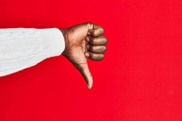 拒絶反応のジェスチャー、不承認嫌いと負の記号をダウン親指を行う赤の隔離された背景にアフリカ系アメリカ人の黒人青年の腕と手  - 写真・画像