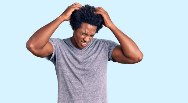 Pohledný africký Američan s afro vlasy na sobě ležérní oblečení trpí bolestí hlavy zoufalý a ve stresu, protože bolest a migréna. Ruce za hlavu.  - Fotografie, Obrázek