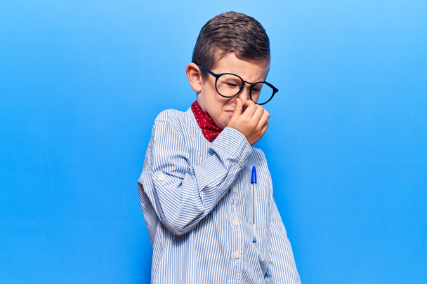 Cute blond kid wearing nerd bow tie and glasses smelling something stinky and disgusting, intolerable smell, holding breath with fingers on nose. bad smell  - Photo, Image