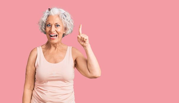 Femme âgée aux cheveux gris portant des vêtements décontractés pointant du doigt avec une idée réussie. Sorti et heureux. numéro un.  - Photo, image