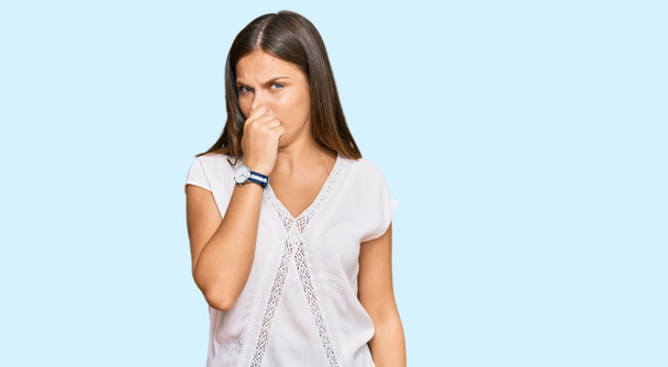 Junge kaukasische Frau in lässiger Kleidung, die etwas Stinkendes und ekelhaften, unerträglichen Geruch riecht und mit den Fingern auf der Nase den Atem anhält. schlechter Geruch  - Foto, Bild