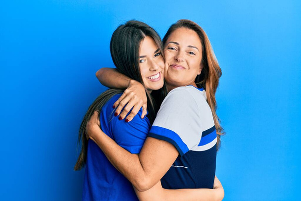 Kaunis latino äiti ja tytär hymyilevä onnellinen halaus yli eristetty sininen tausta. - Valokuva, kuva
