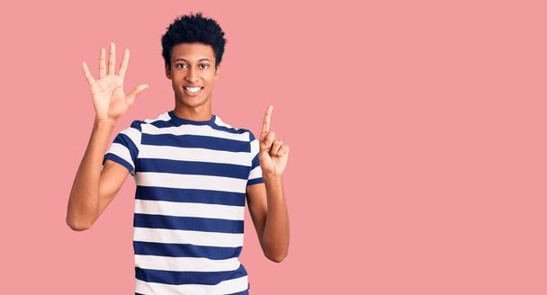 Молодий афроамериканець, одягнений у повсякденний одяг, показує і вказує вгору з пальцями номер шість, посміхаючись впевнено і щасливо.  - Фото, зображення