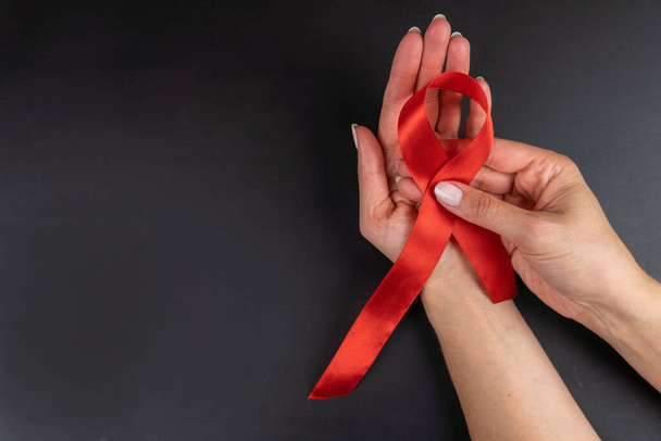 Manos femeninas con cinta roja VIH, cinta de sensibilización sobre el sida, concepto de salud y medicina. espacio de copia. - Foto, imagen