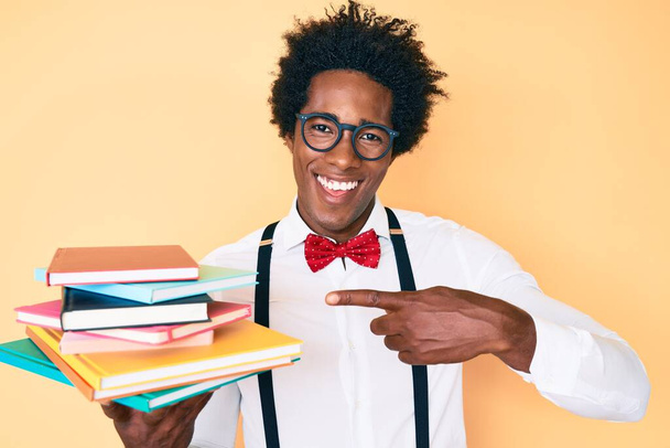 Handsome african american nerd man with afro hair holding books smiling happy pointing with hand and finger  - Foto, Imagem