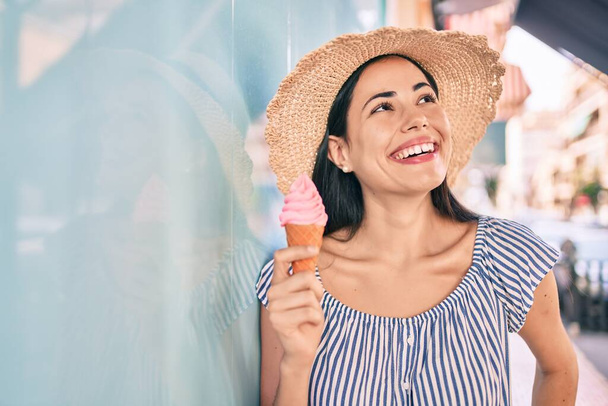 Młoda latynoska turystka na wakacjach uśmiechnięta szczęśliwa jedząc lody w mieście. - Zdjęcie, obraz