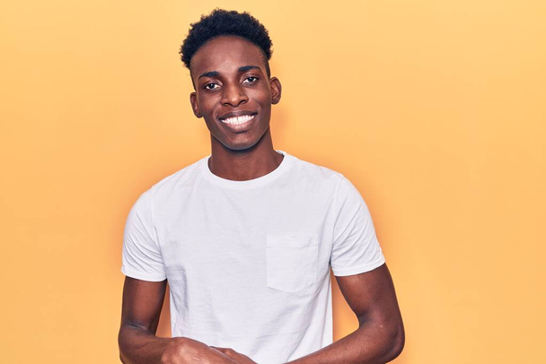 Junger afrikanisch-amerikanischer Mann in lässiger Kleidung mit zusammengelegten Händen und erhobenen Fingern, der entspannt und fröhlich lächelt. Erfolg und Optimismus  - Foto, Bild