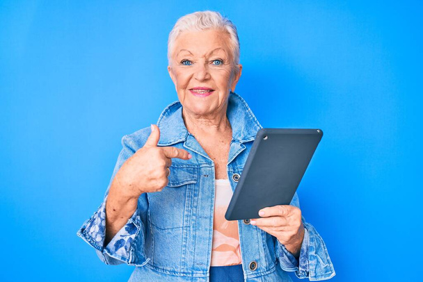 Senior mooie vrouw met blauwe ogen en grijs haar met behulp van touchpad apparaat wijzende vinger naar een zelf lachende gelukkig en trots  - Foto, afbeelding